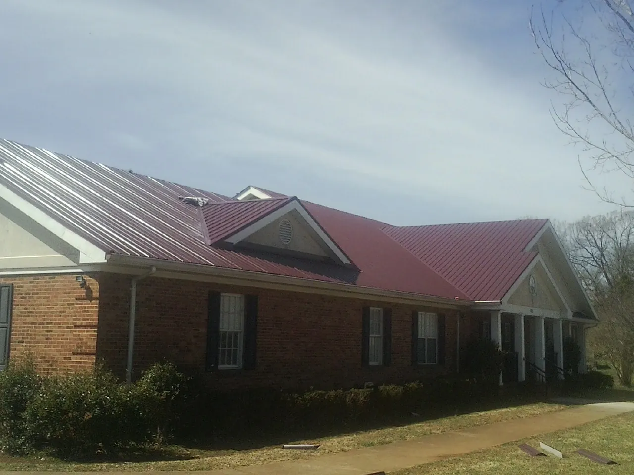 Red metal roof with gabled entries on a long brick building, from a Hail Damage Roof Repair job in Saint Johnsbury