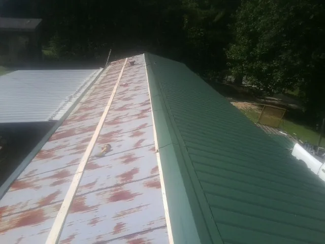 Old rusted panels beside newly installed green metal roofing — Wind Damage Roof Repair by Roofing Brothers in Saint Johnsbury
