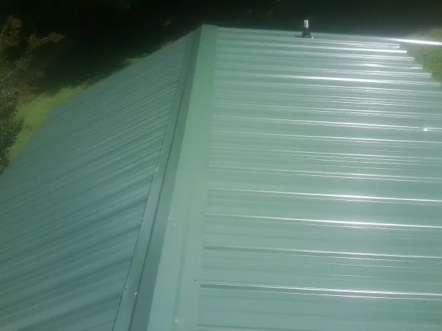 New green metal panels meeting at the ridge of a roof — Flat Roof Repair work by our crew in Saint Johnsbury