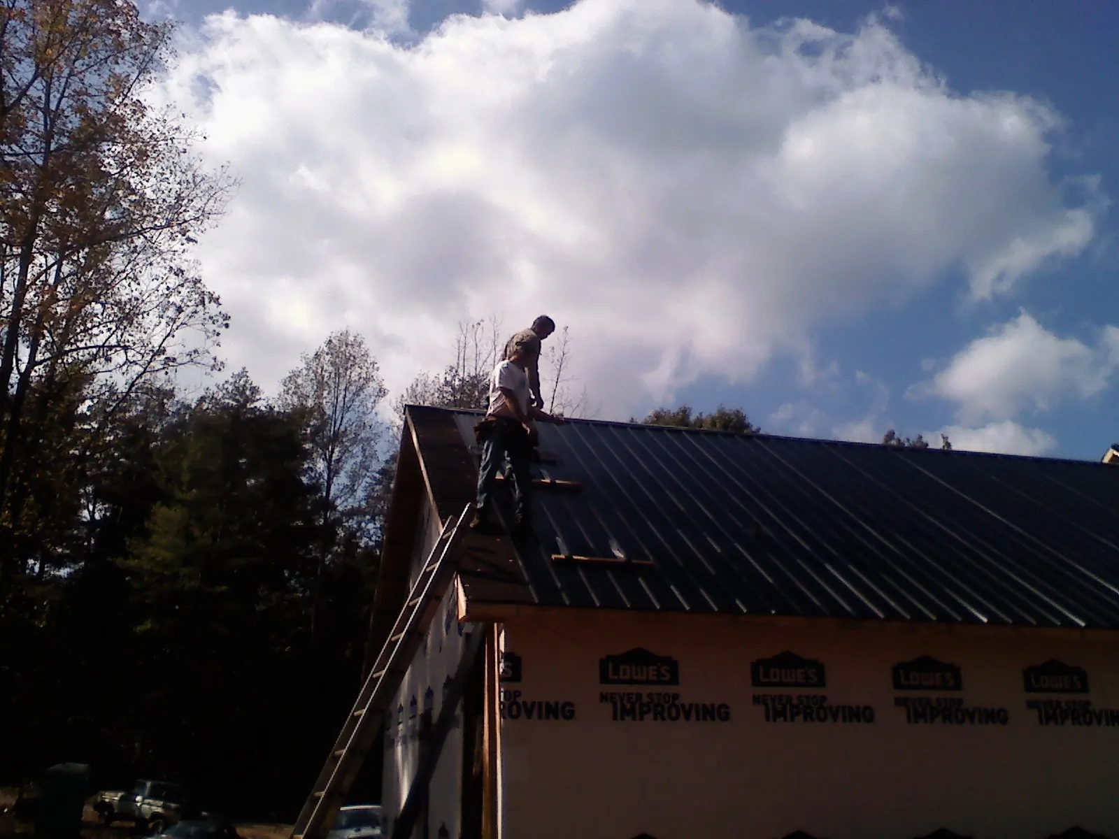 Roofer fastening dark metal panels high against a cloudy sky, from a Roof Inspection job in Saint Johnsbury