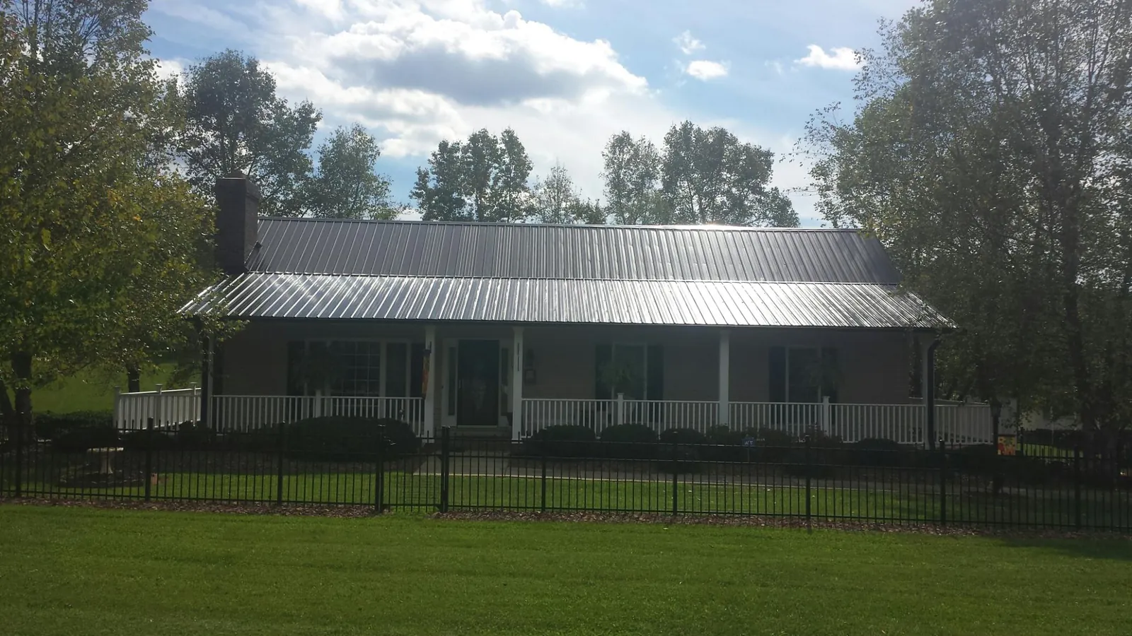 Gray metal roof on a brick ranch with a full width front porch — Gutter Guard Installation work by our crew in Saint Johnsbury