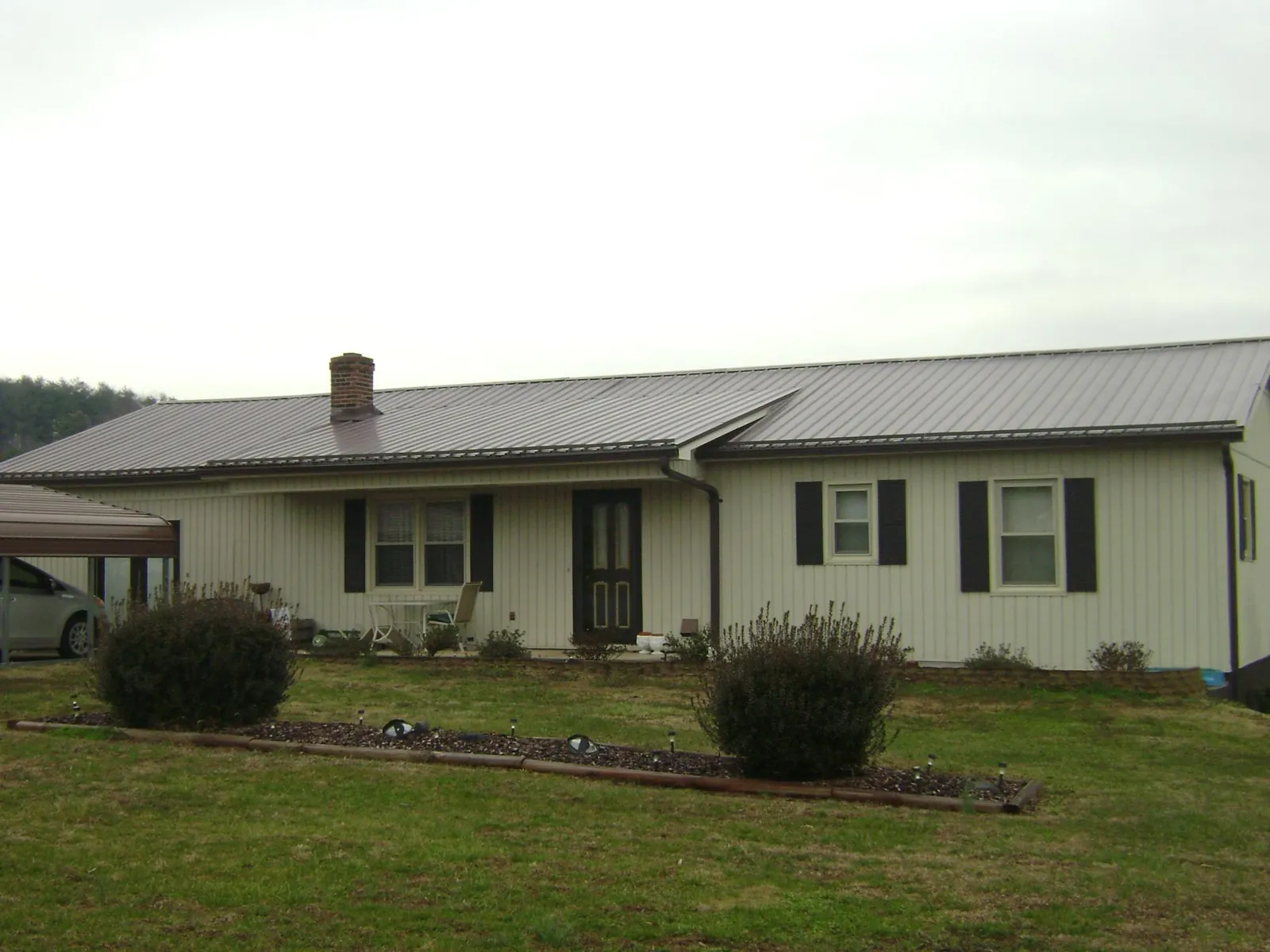 Brown metal roof on a cream sided ranch home with a brick chimney in Saint Johnsbury