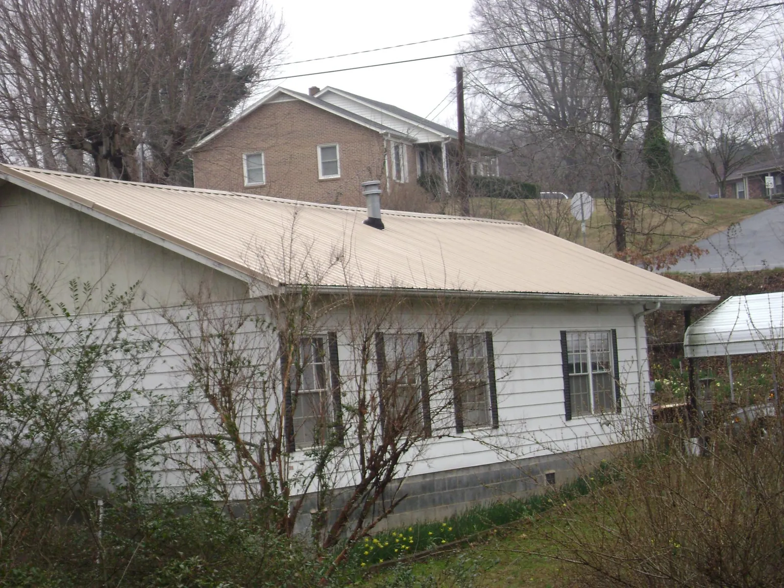 Tan metal roof on a white sided house set into a hillside — Commercial Roofing by Roofing Brothers in Saint Johnsbury