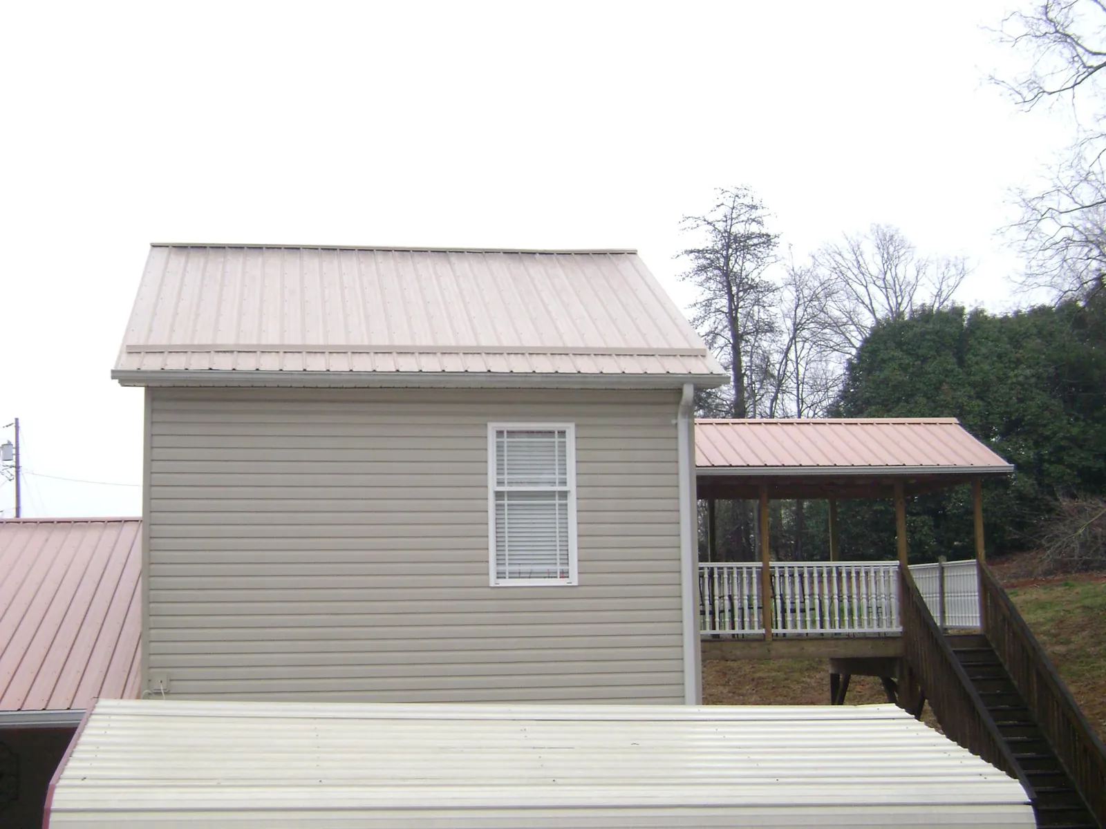 Tan metal roofs on a two story addition and attached porch, from a Roof Replacement job in Saint Johnsbury